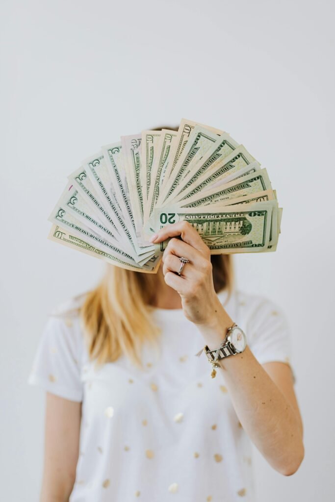 pexels-photo-4968648-4968648 Woman holding a fan of US dollar bills in front of her face.
